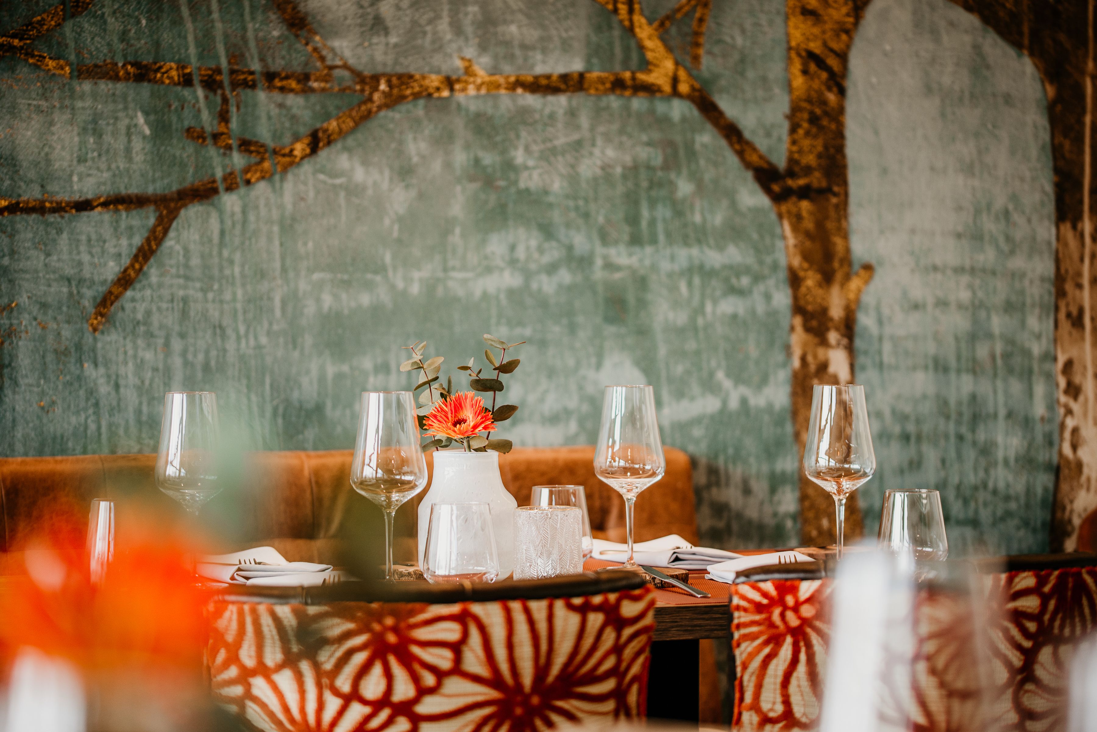 A dining table set with wine glasses, a vase with flowers, and a patterned table runner.