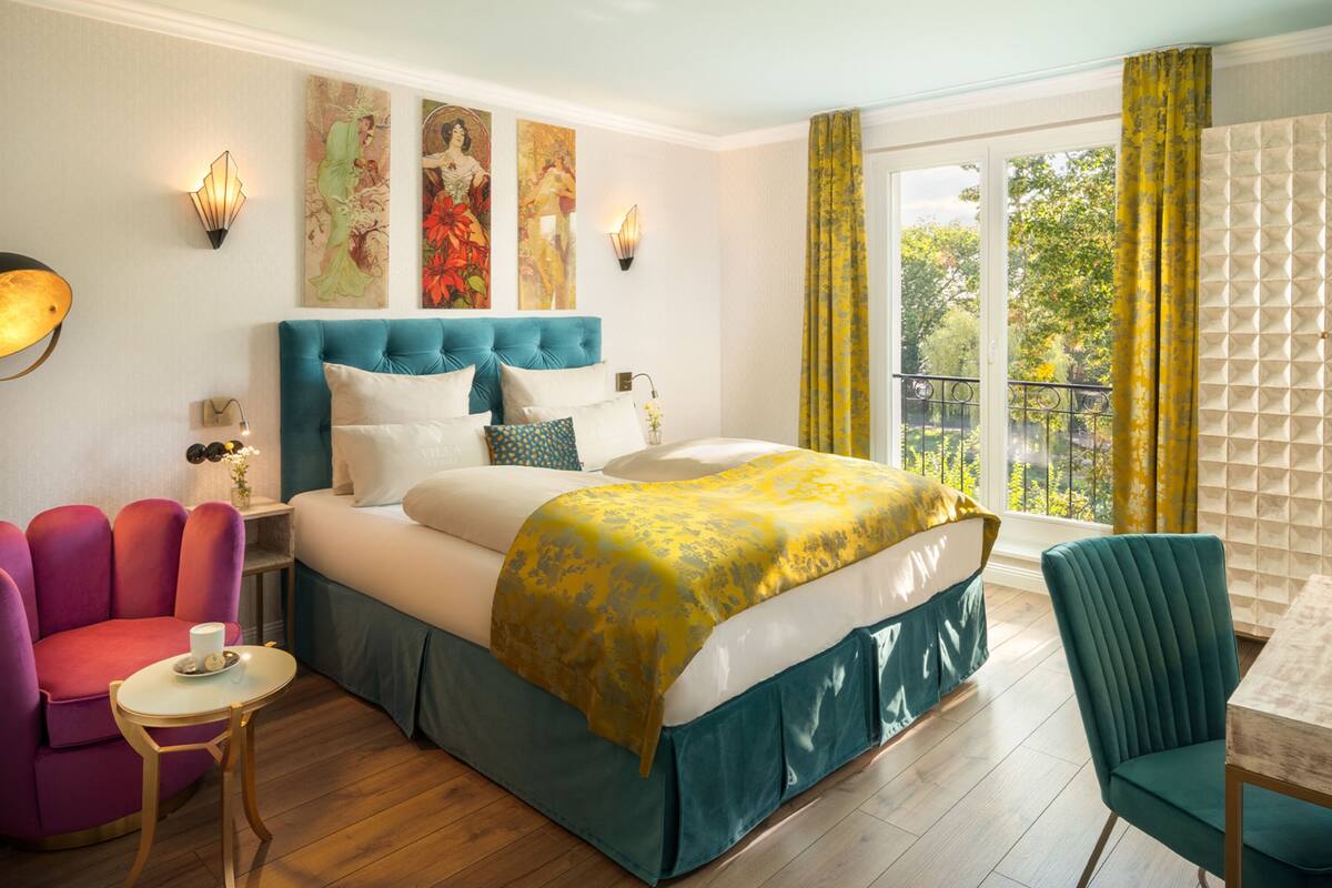 A hotel room with a large bed, a sitting area with a chair and table, and artwork on the walls.
