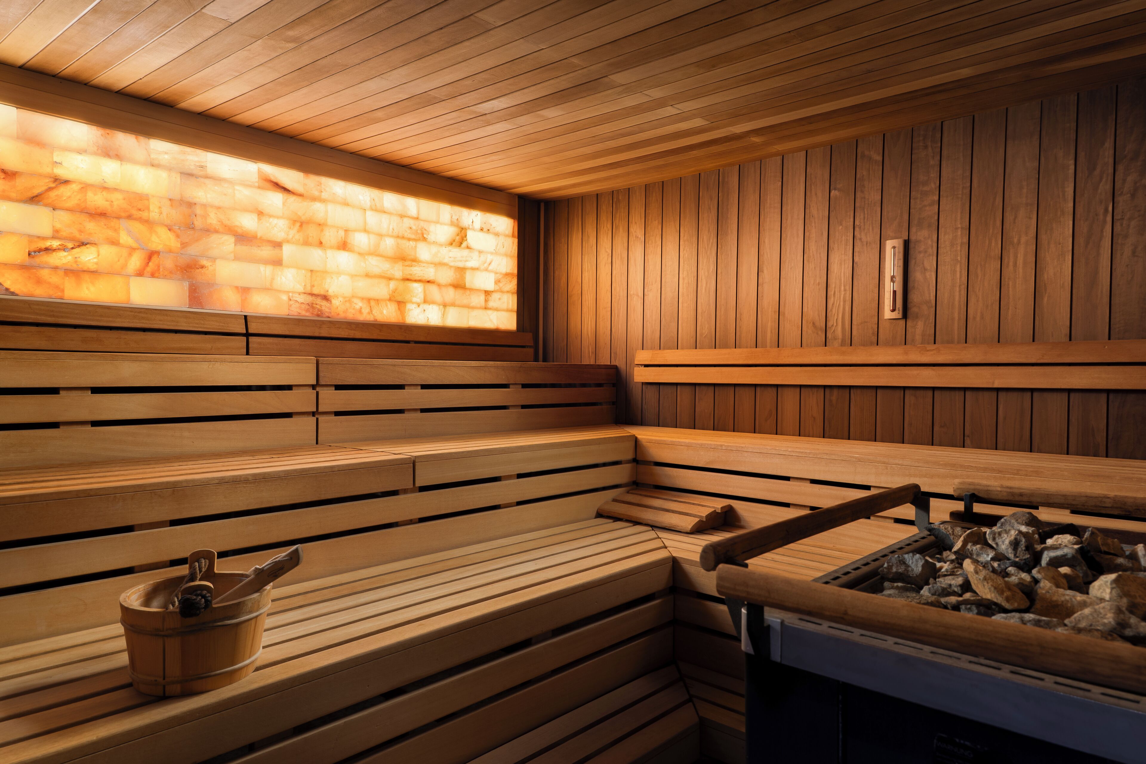 Una sauna con bancos de madera, una pila de piedra y una pared de madera con ventana.