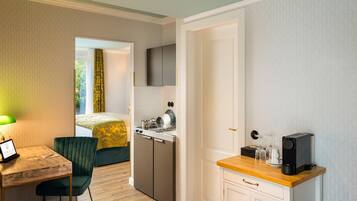 A compact hotel room with a bed, a desk with a chair, a kitchenette, and a TV mounted on the wall.