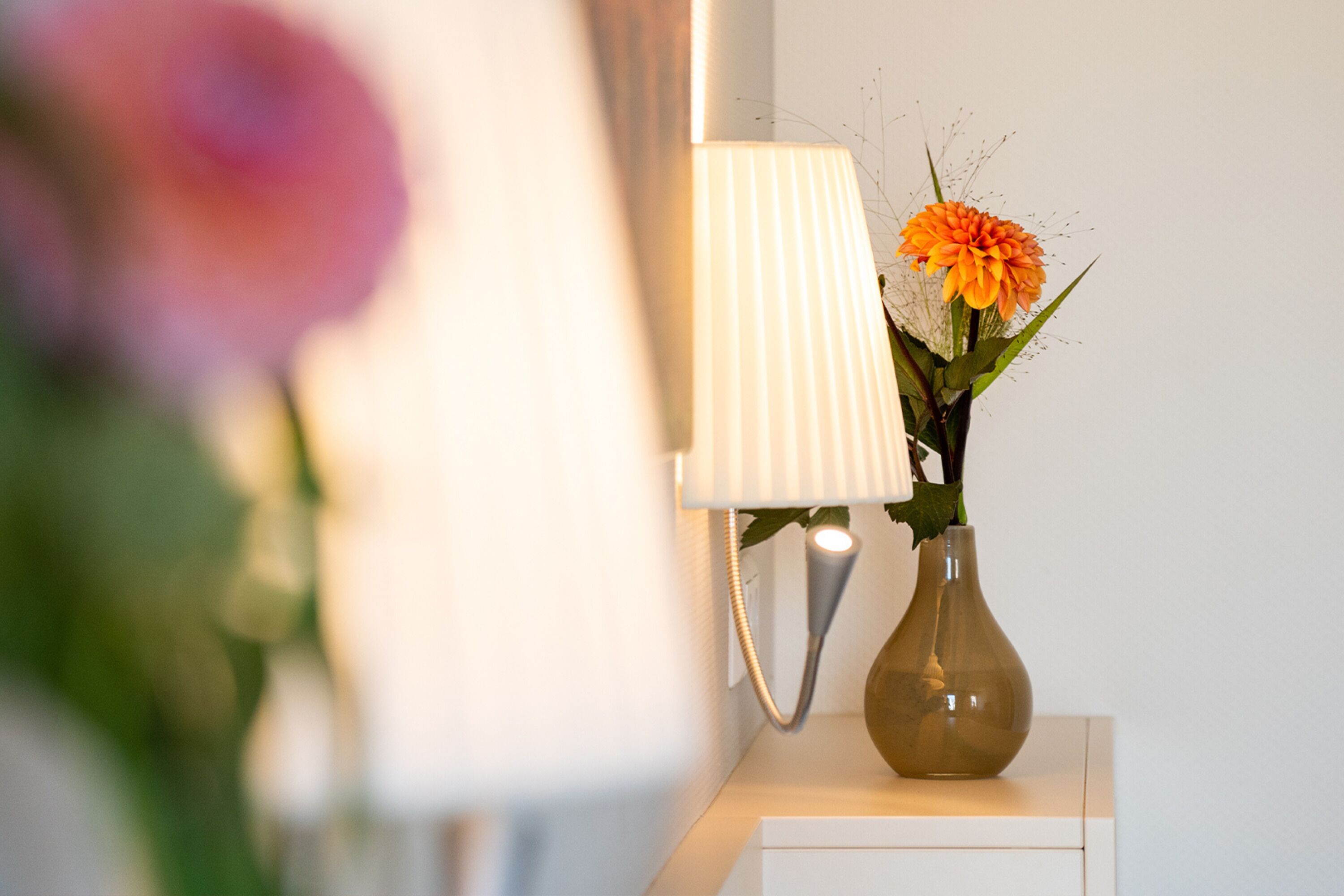 A lamp with a white shade and a vase with flowers on a white surface.