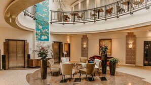 A spacious lobby with a curved marble floor, a central seating area with chairs, a reception desk, and a large vertical floral mural.