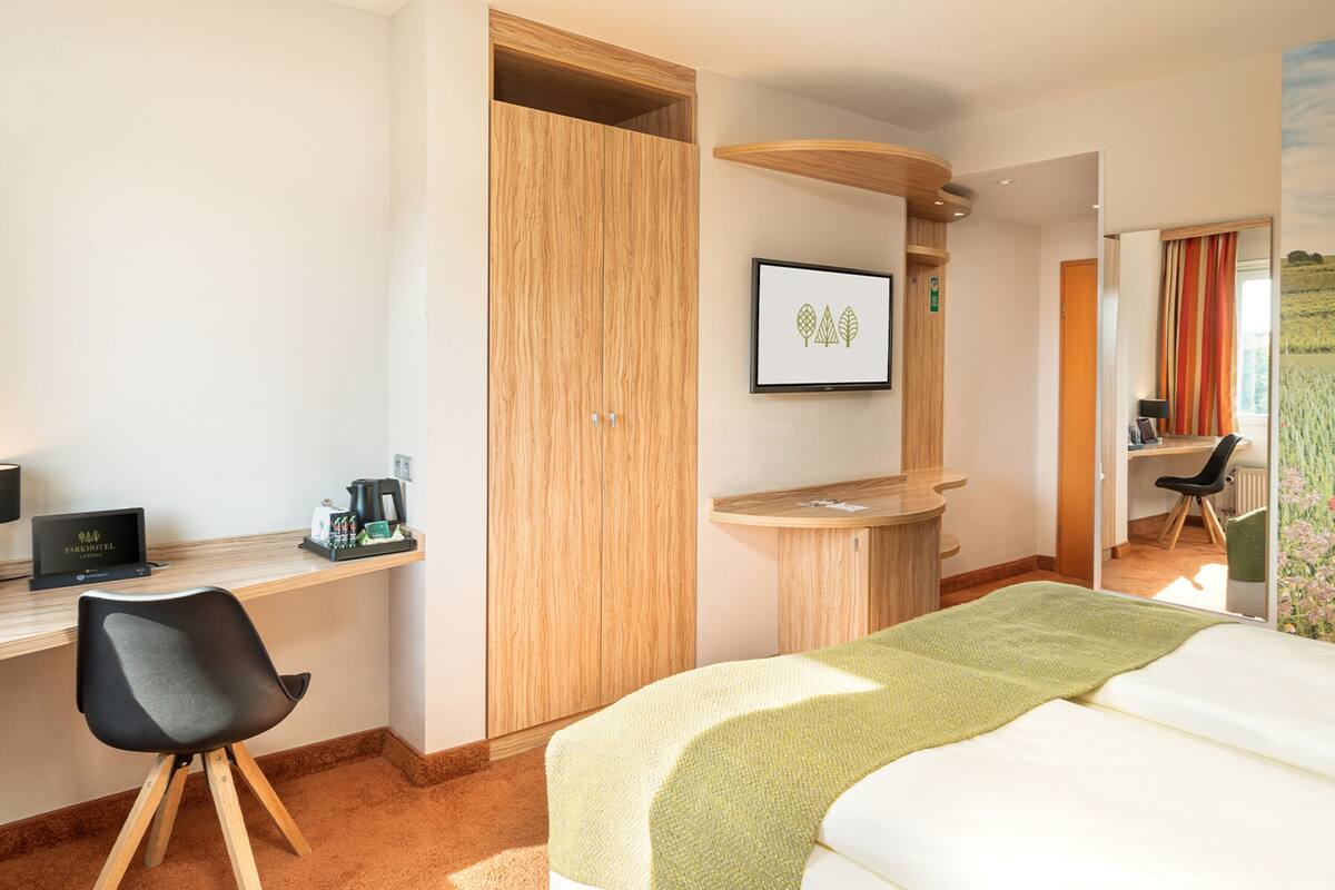 A hotel room with a bed, desk, chair, and a view of a field through the window.