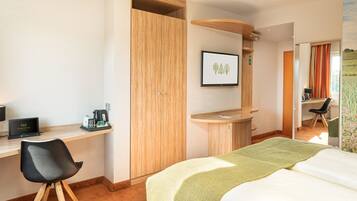 Ein Hotelzimmer mit Bett, Schreibtisch, Stuhl und Blick auf ein Feld durch das Fenster.