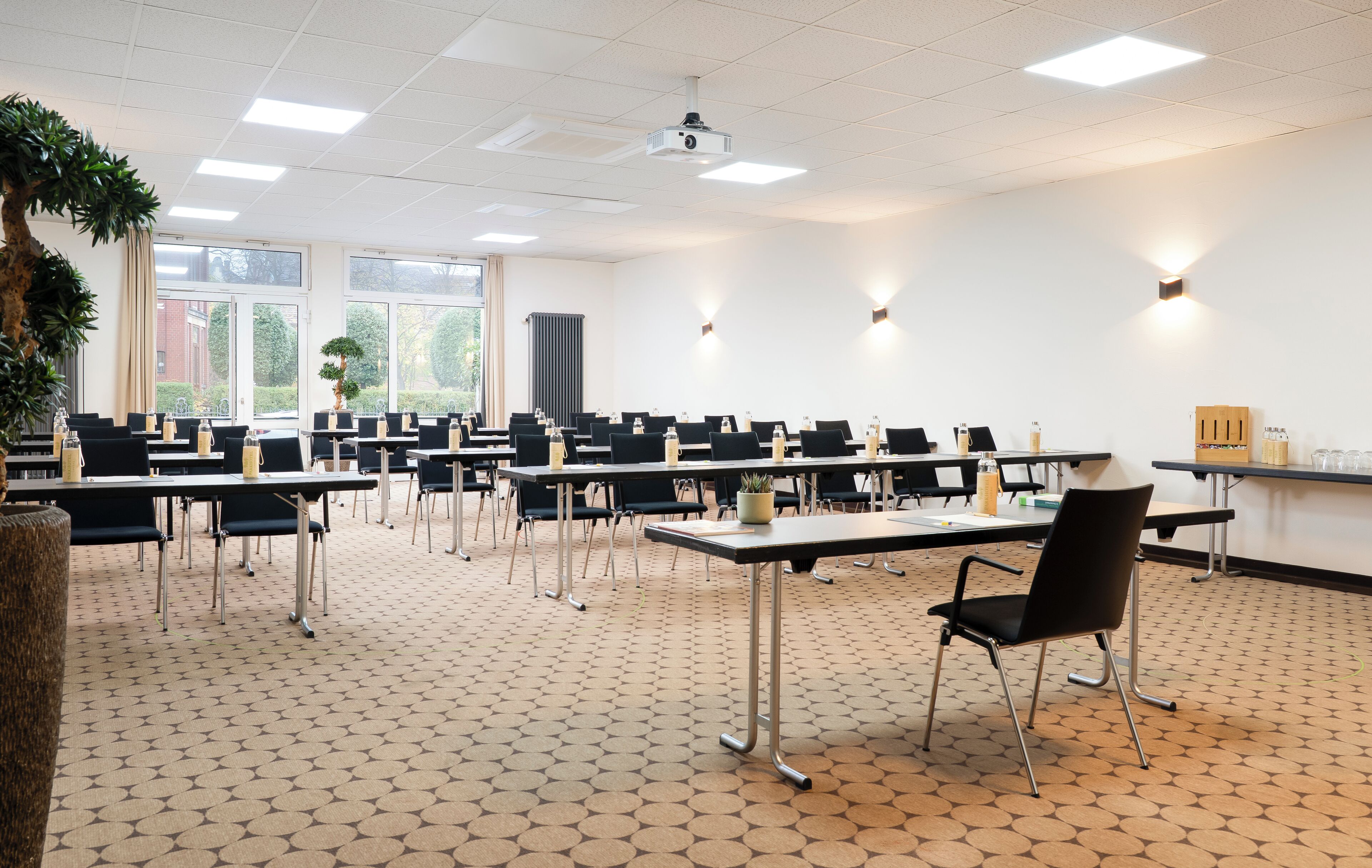 A conference room with multiple tables and chairs, large windows, and a projector on the ceiling.