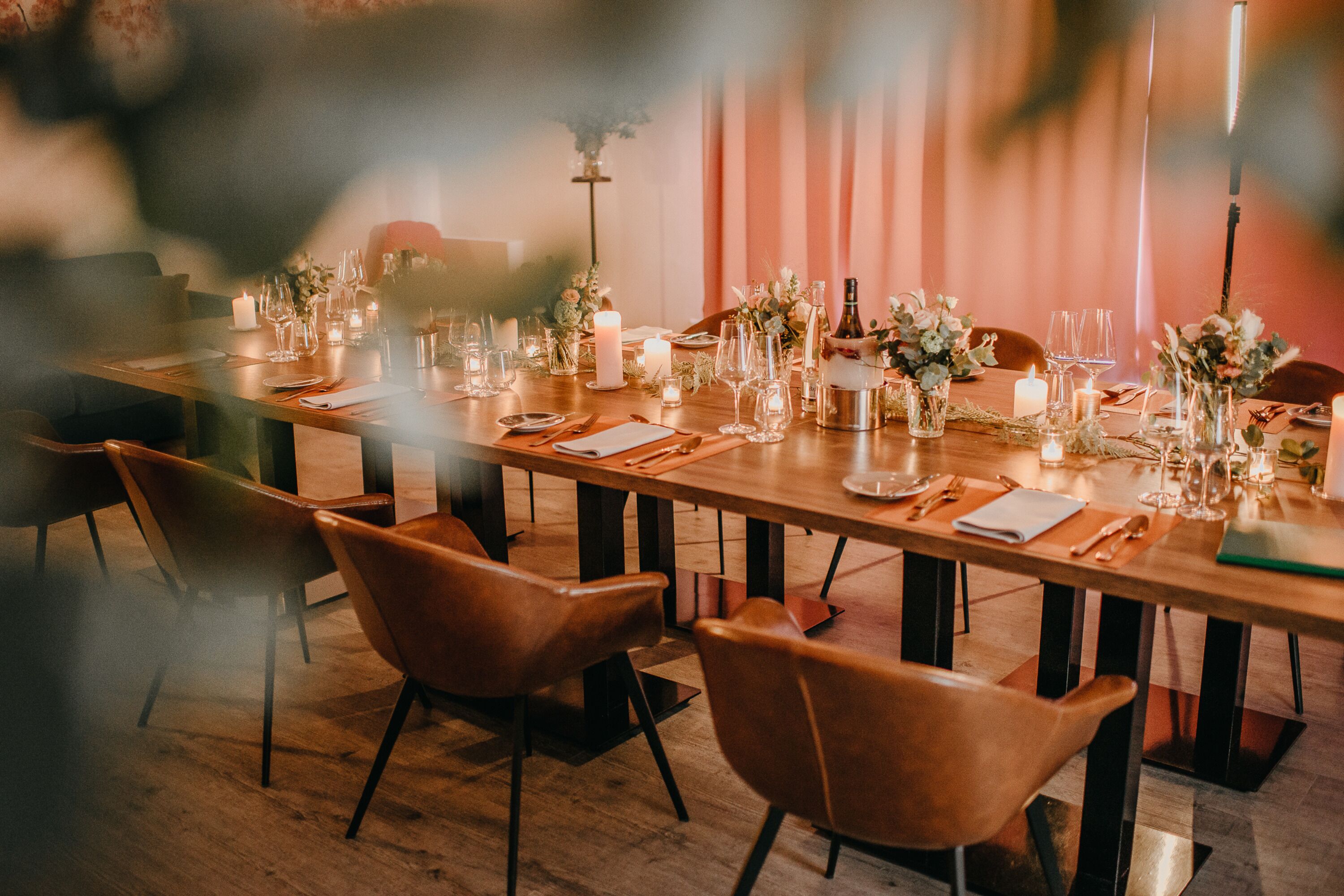 A long dining table set with candles, glassware, and floral centerpieces, surrounded by leather chairs.