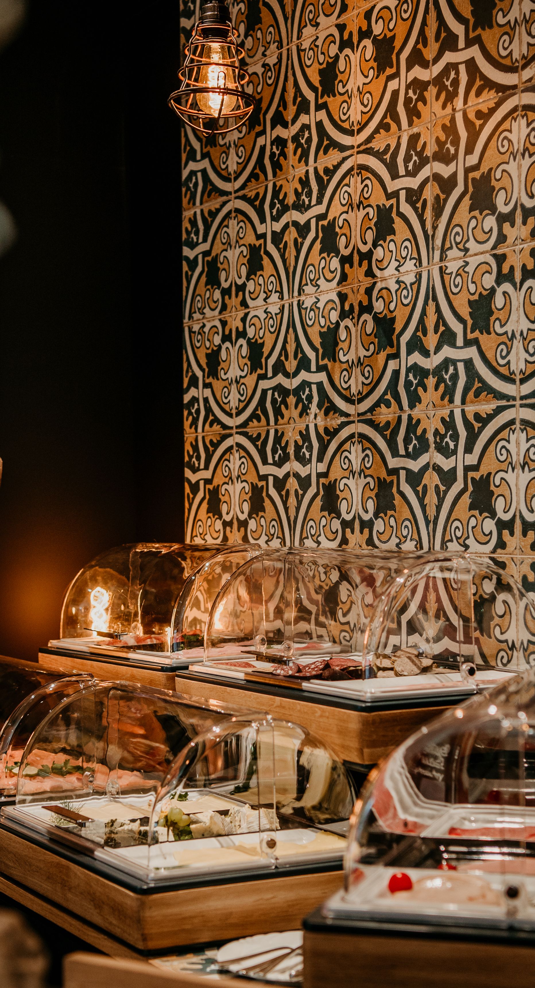 A buffet area with glass-covered food displays, a patterned wall, and a hanging light fixture.