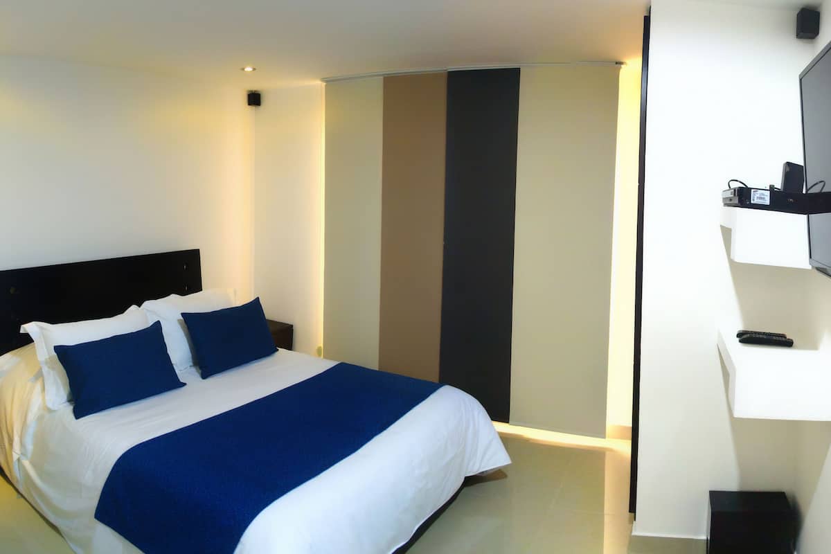 A hotel room with a bed, a TV mounted on the wall, and a door with a vertical stripe pattern.