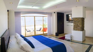 Una habitación de hotel moderna con una cama grande, una chimenea de piedra, un balcón con una silla y un televisor montado en la pared.