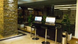 Zona de recepción con un pilar de piedra, dos taburetes de bar y dos computadoras portátiles sobre una encimera negra.