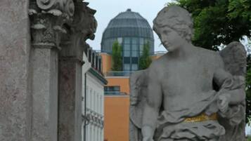 A statue of an angel with a child, set against a building with a dome and a tree in the background.