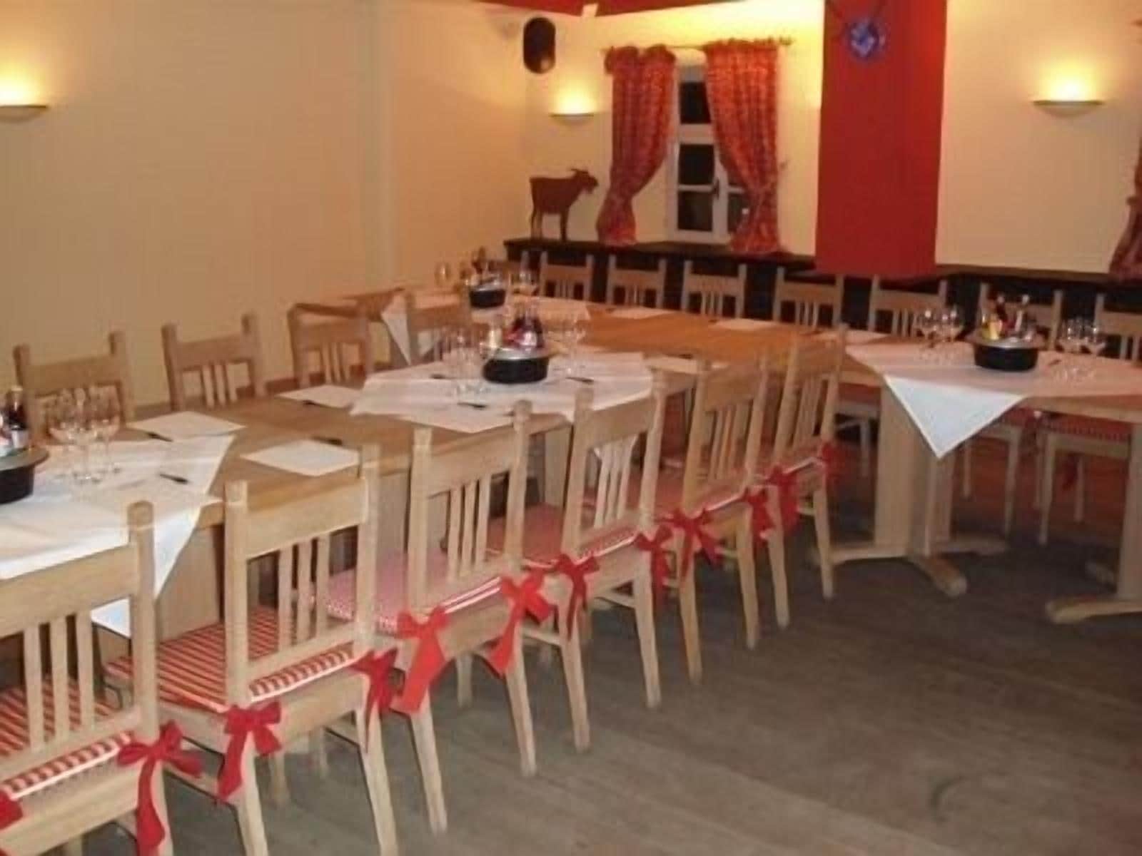 A dining area with wooden tables and chairs, red bows on the chairs, and a red wall.