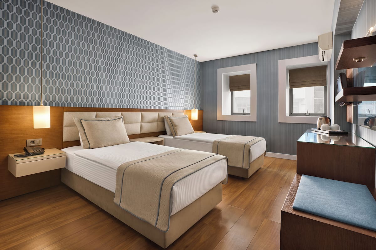 A hotel room with two beds, a desk, a chair, and a window.