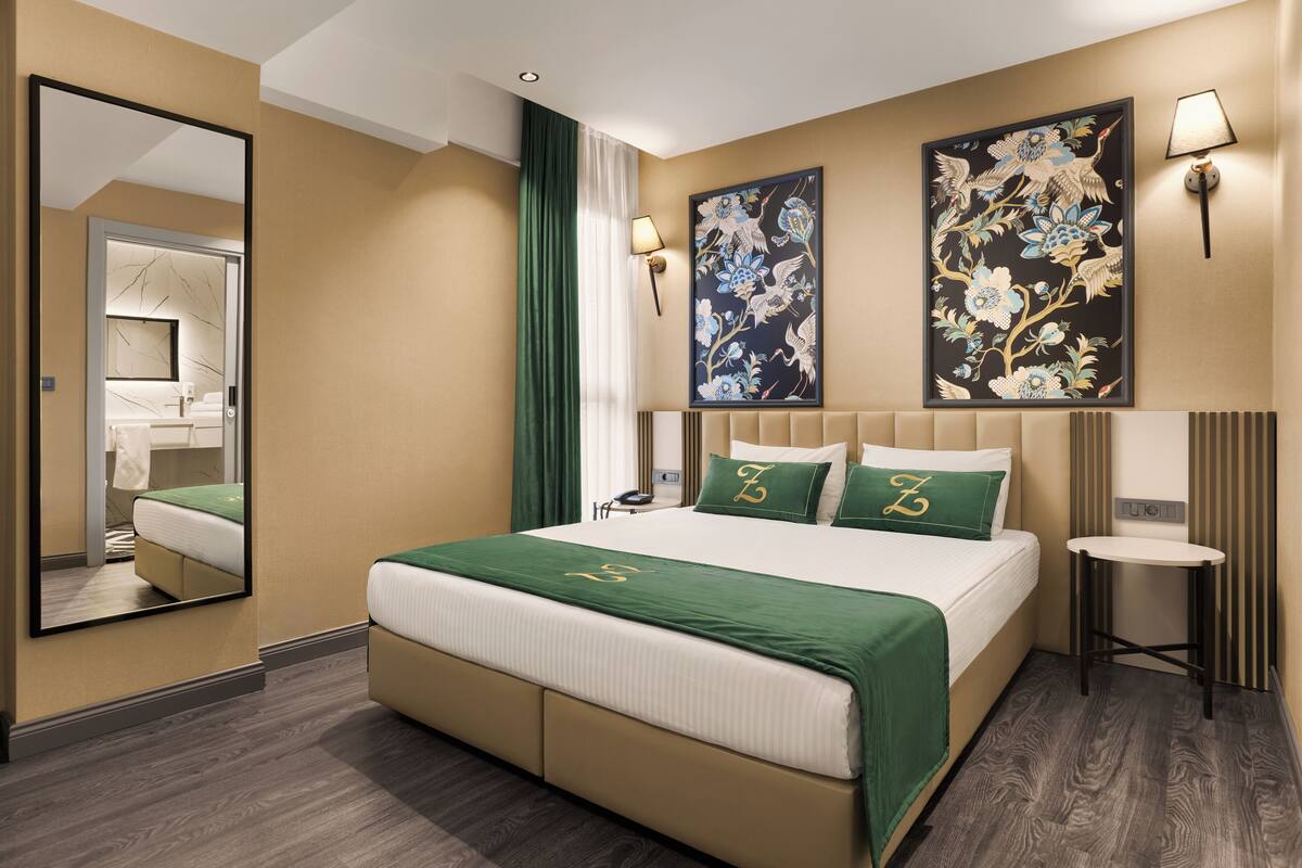 A hotel room with a large bed, two wall-mounted lamps, a mirror, and two framed floral artworks.
