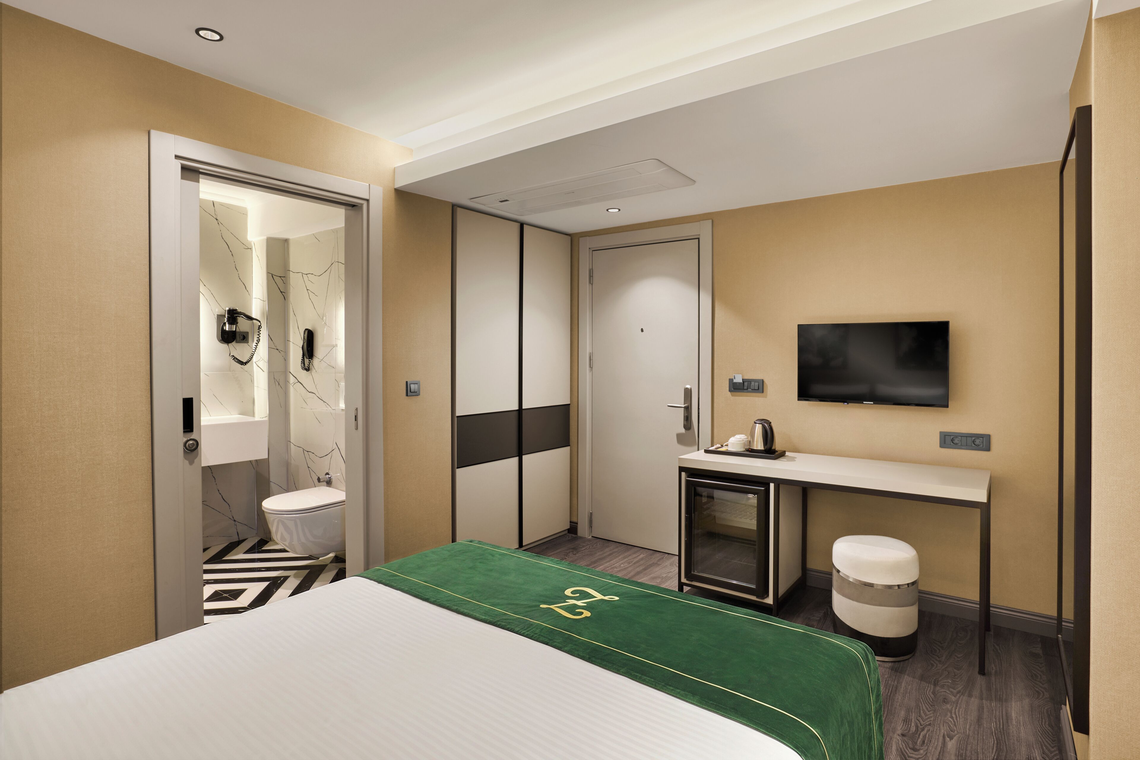 A hotel room with a bed, a desk, a TV, a mirror, a toilet, and a trash bin.