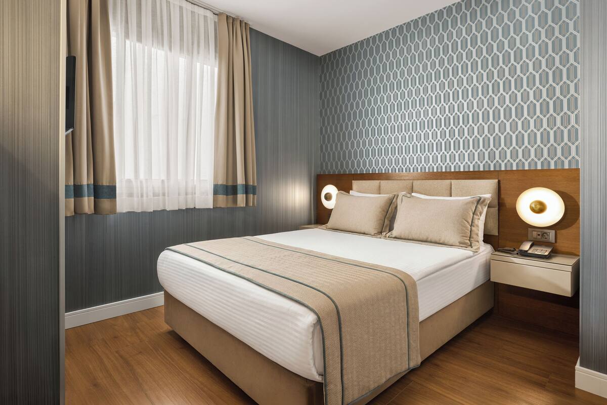 A hotel room with a bed, nightstand, and wall-mounted lamp.