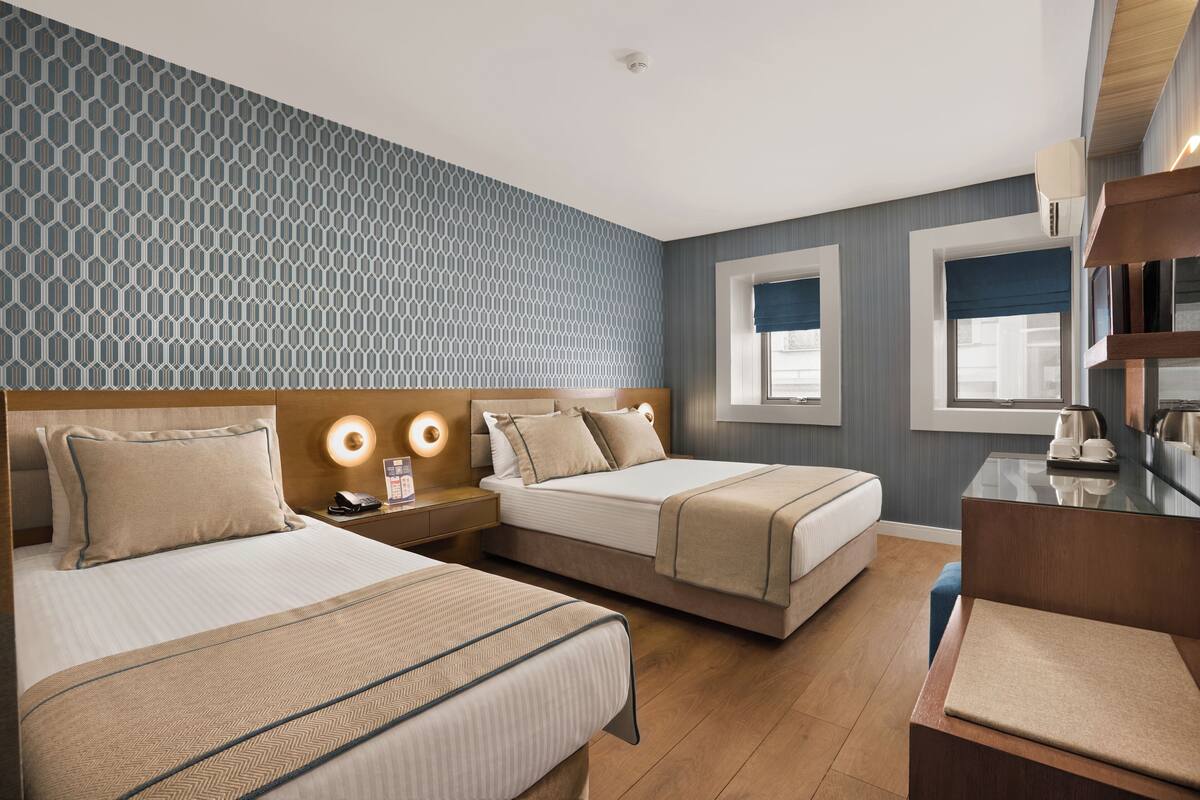 A hotel room with two beds, a desk, a chair, and a window with a view.