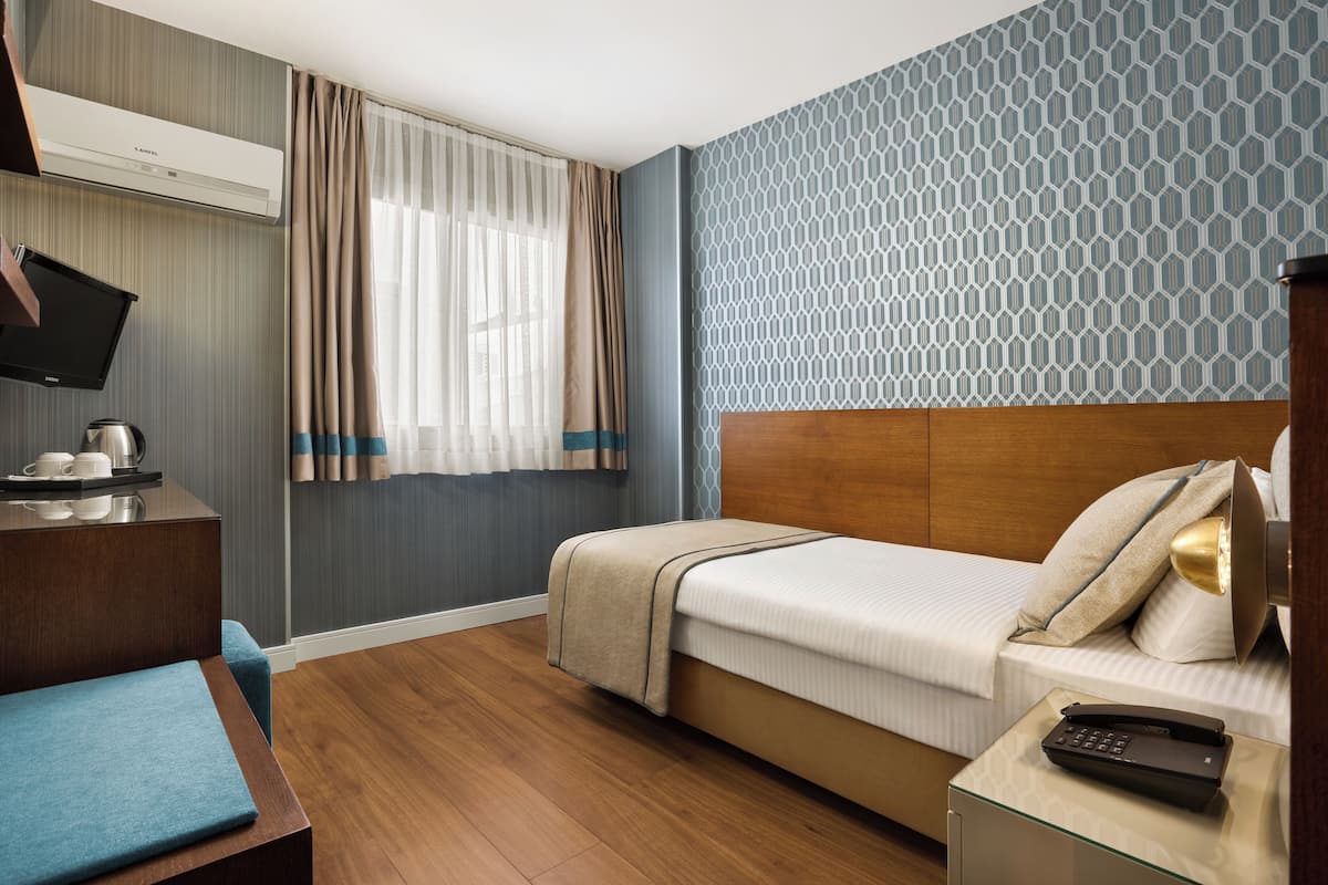 A hotel room with a bed, bedside table, TV, and a window with curtains.