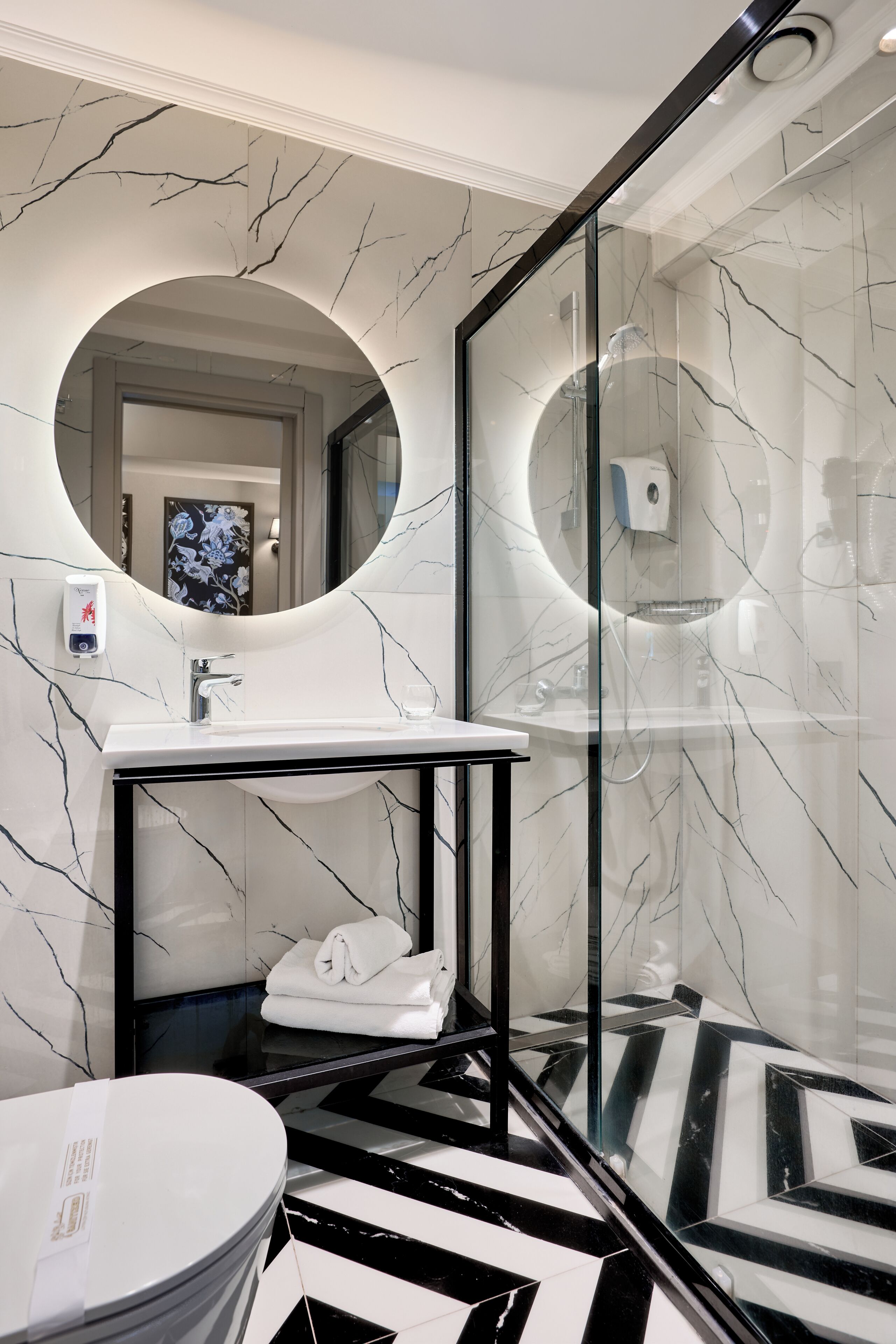 A modern bathroom with a marble vanity, a round mirror, and a black and white patterned floor.