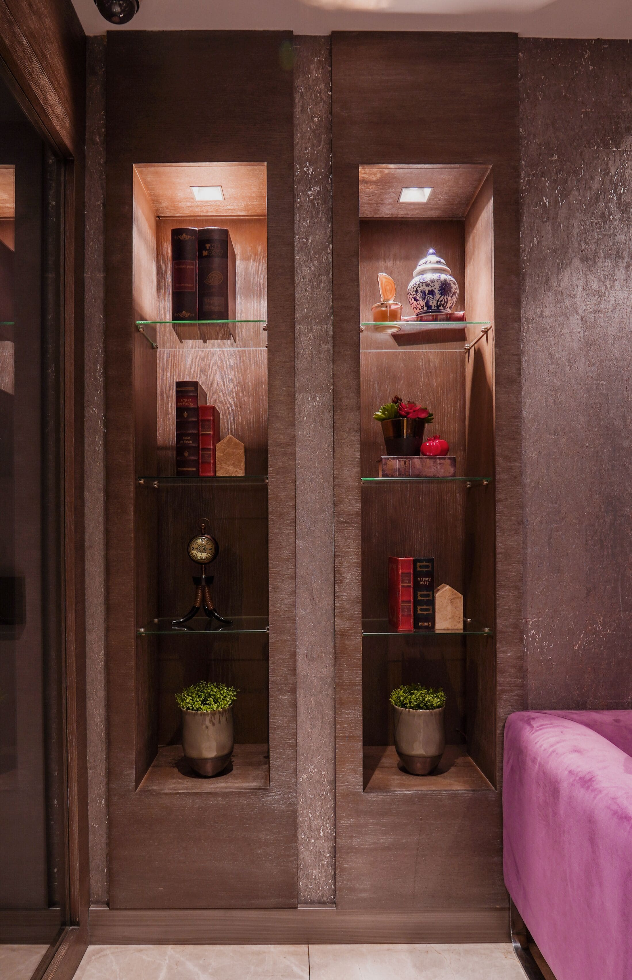 Una habitación con dos estanterías de madera, cada una con libros, objetos decorativos y plantas en macetas.