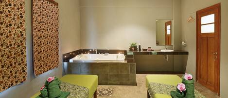 A spa room with two massage tables, a large bathtub, and a sink.