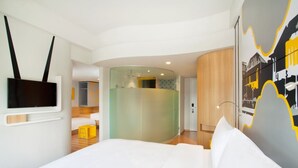 Een moderne hotelkamer met een gebogen glazen scheiding, een flatscreen televisie aan de muur, een bed met witte lakens en een minimalistisch design.