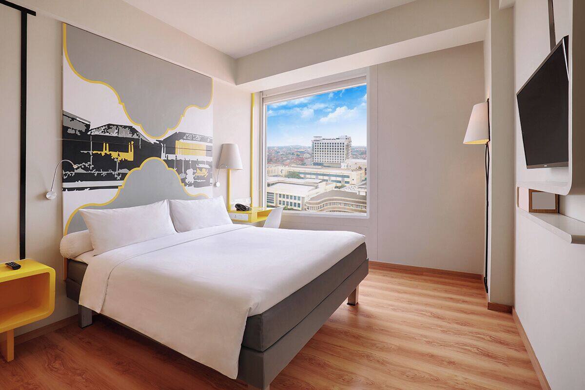 A modern hotel room with a large bed, a city view, a flat-screen TV, and a minimalist decor.