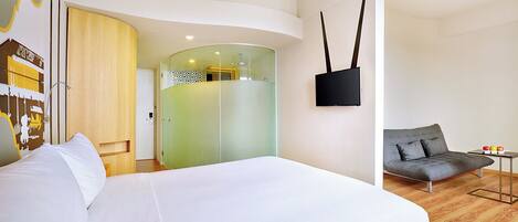 A modern hotel room with a large bed, a sofa, a flat-screen TV, and a glass partition wall.