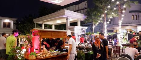 An outdoor dining area with a food stall, tables, and chairs.