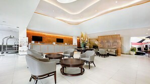 Een moderne hotel lobby met een receptiebalie, een zithoek en een decoratieve plant.