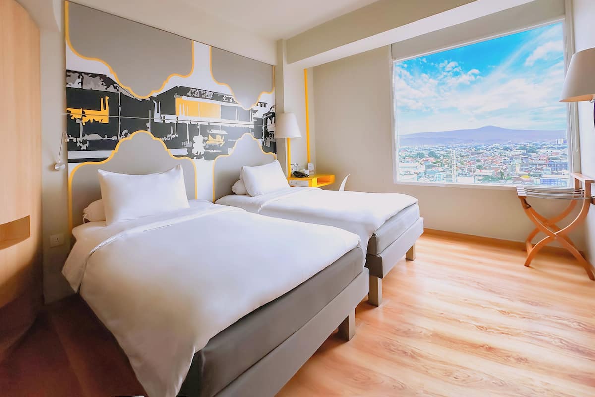 A hotel room with two beds, a large window with a city view, and a wall mural.