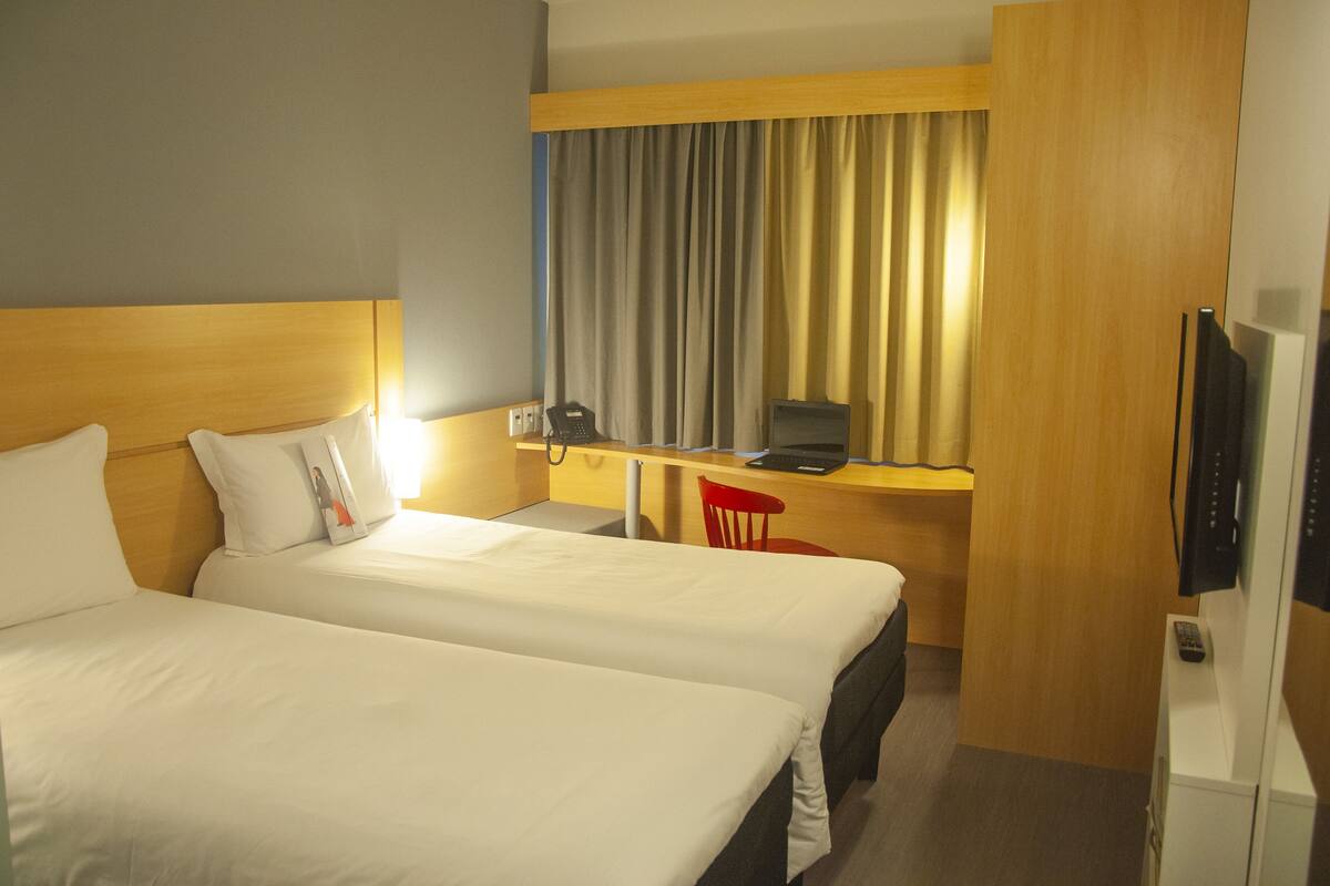 Una habitación de hotel con dos camas, un escritorio con una silla, un televisor y un teléfono.