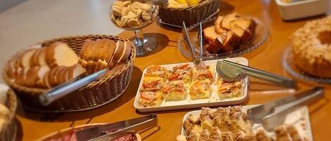 A buffet table with various food items including bread, pastries, fruits, and desserts.