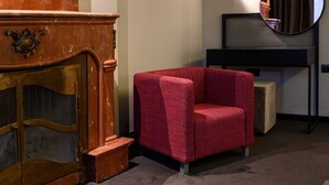 A room with a wooden cabinet, a red armchair, a round mirror, and a black shelf. - Artloft Hotel (Nis)