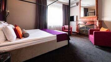 Una camera d'albergo con un letto, una poltrona rossa, un caminetto e un grande specchio.
