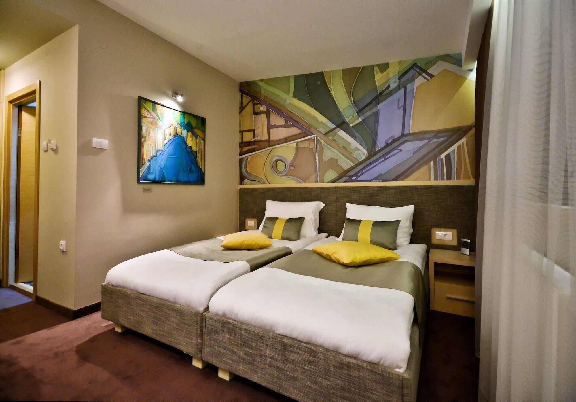 A hotel room with two beds, a painting on the wall, and a nightstand with a lamp.