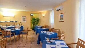 Un espace repas avec des tables dressées pour les repas, des chaises et une plante en pot.