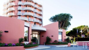 Un hôtel moderne à la façade rose, doté de nombreux balcons et orné d’un grand arbre au premier plan.