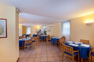 A dining area with tables and chairs, a potted plant, and a framed picture on the wall.