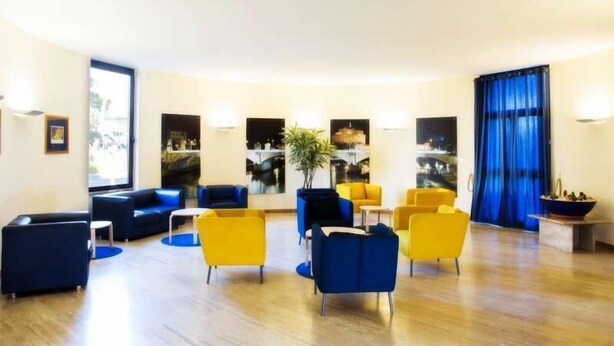 Un hall d’entrée moderne avec des sièges bleus et jaunes, de grandes fenêtres et un rideau bleu.