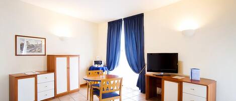 Una habitación pequeña y limpia con una cama, un escritorio, una silla, un televisor y una ventana con cortinas.