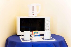 Un forno a microonde con una caffettiera sopra, due tazze bianche e una scatola di tè su un tavolo con una tovaglia blu.
