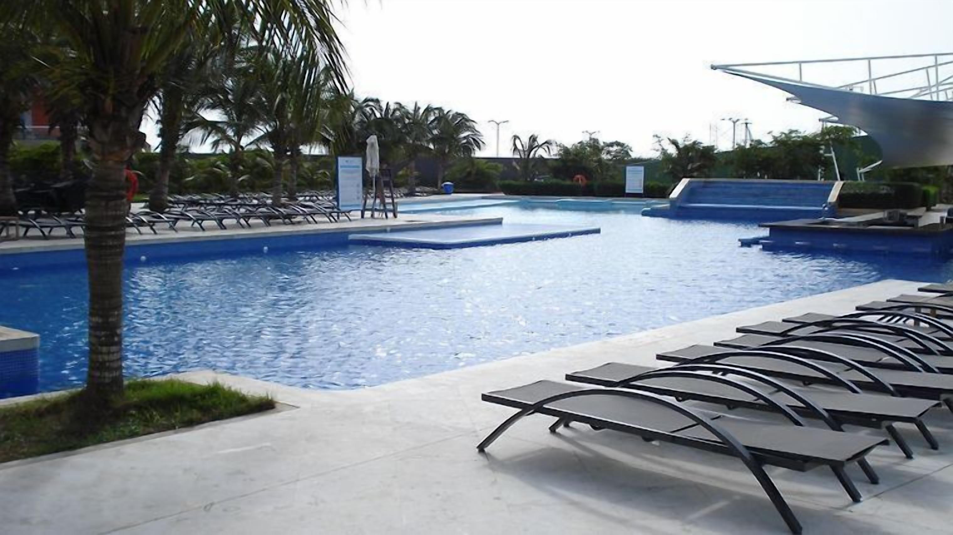A swimming pool with lounge chairs, palm trees, and a modern architectural structure in the background.