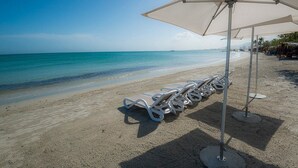 Una playa con sillas y sombrillas blancas, una orilla arenosa y un mar tranquilo al fondo.