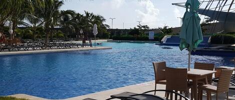 A pool area with lounge chairs and umbrellas, surrounded by palm trees.