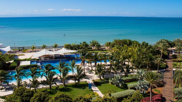 Un resort con una gran piscina, palmeras y vistas al océano.