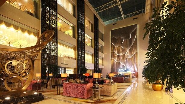 A spacious lobby with high ceilings, multiple seating areas, and a large decorative sculpture. - Wyndham Grand Plaza Royale Changsheng Jiangyin (Wuxi)