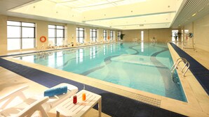An indoor swimming pool with clear blue water, white lounge chairs, and a lifebuoy on the wall. - Wyndham Grand Plaza Royale Changsheng Jiangyin (Wuxi)