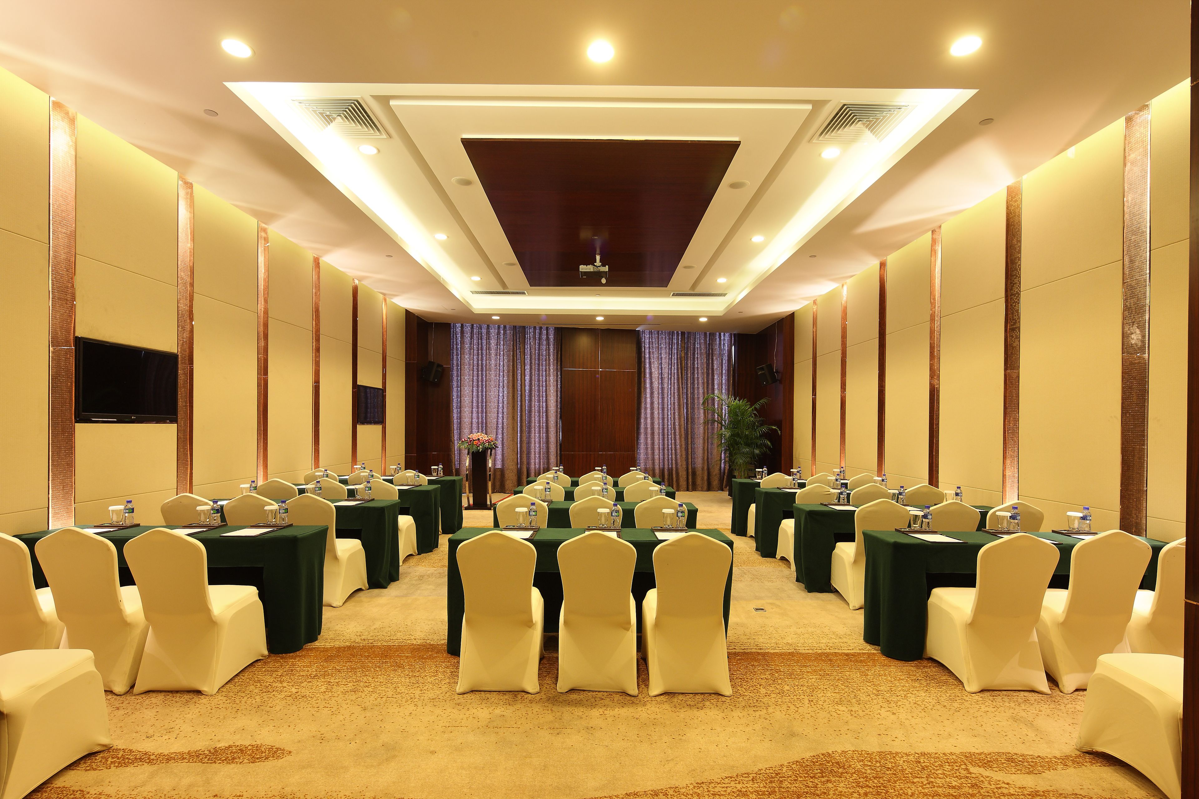 A conference room with multiple tables and chairs, equipped with water bottles and nameplates, and a large screen at the front.