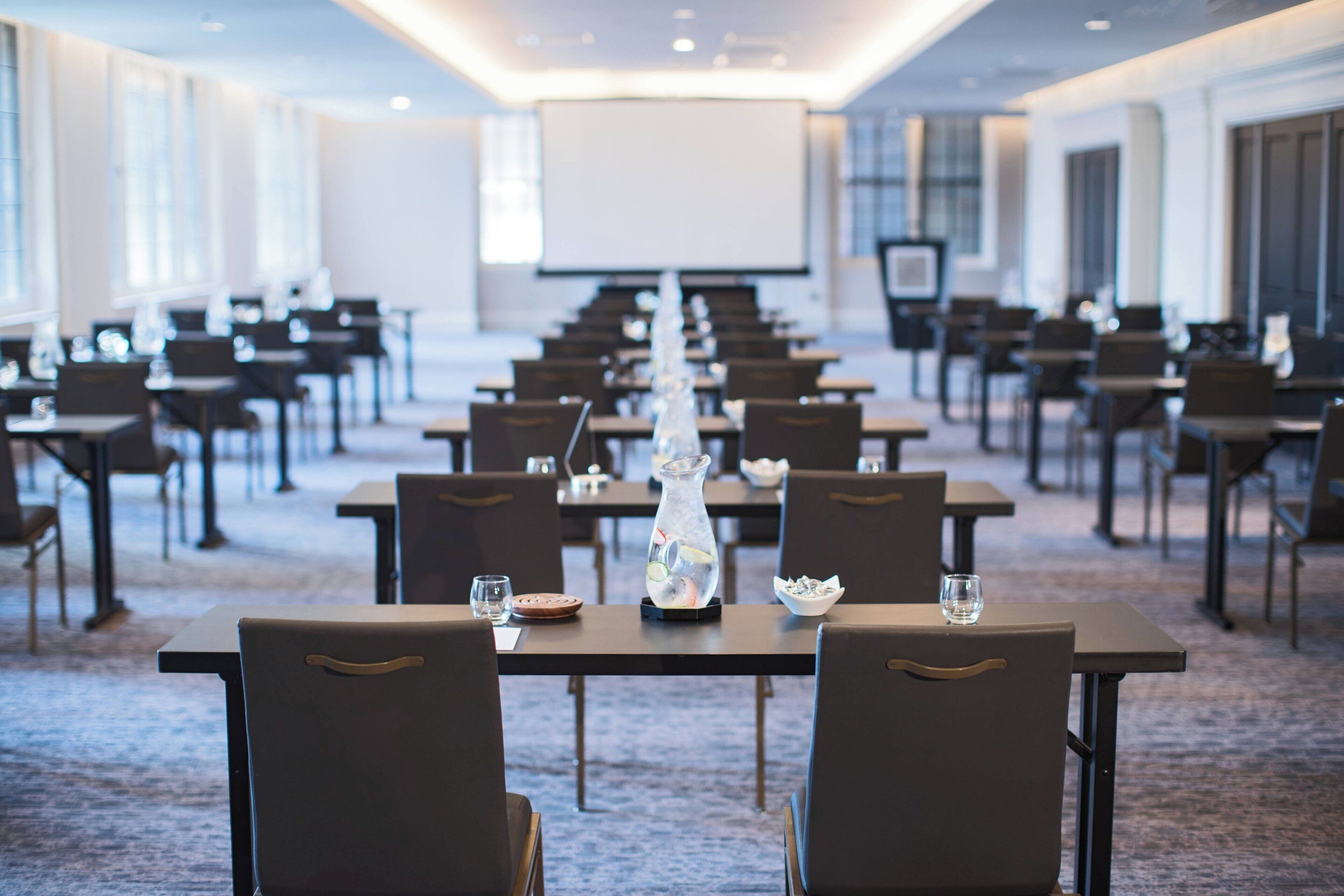 A conference room with rows of tables and chairs, a projector screen, and a large window.